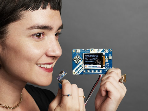 Smiling woman holding up TensorFlowLite microcontroller computer chip. Photo credit: Adafruit